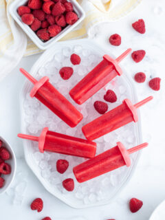 five raspberry popsicles laid on a bowl of ice cubes