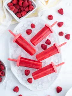 five raspberry popsicles laid on a bowl of ice cubes