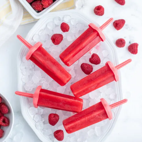 five raspberry popsicles laid on a bowl of ice cubes