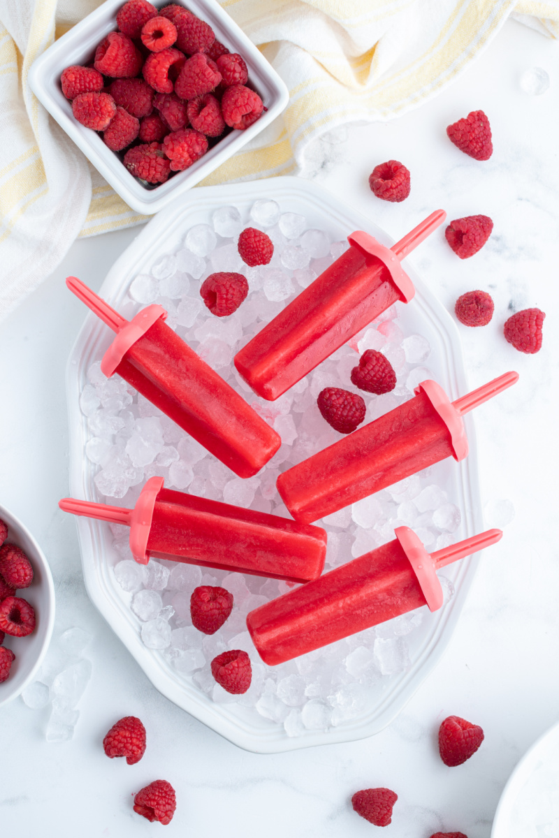 five raspberry popsicles laid on a bowl of ice cubes