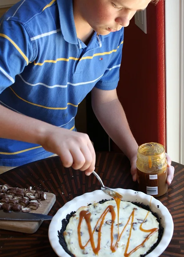 Drizzling caramel topping on the Twix Bar Cheesecake Pie