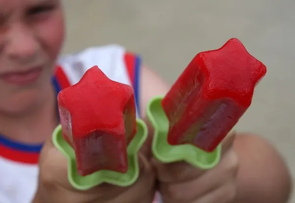 little boy holding two raspberry popsicles at camera