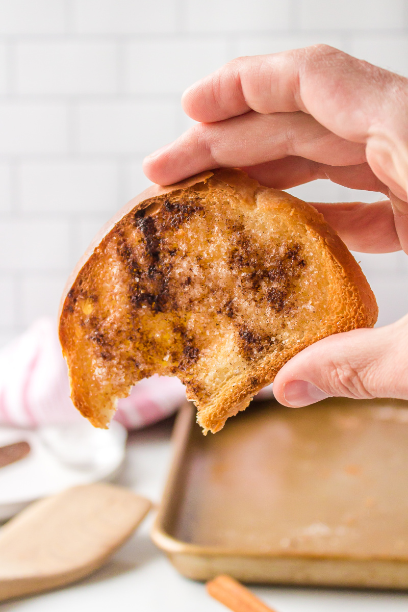 hand holding piece of cinnamon toast with bite taken out of it