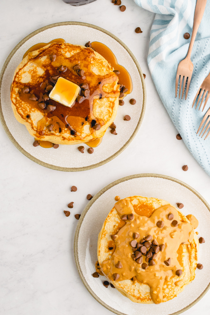 two stacks of pancakes with syrup on one and peanut butter on another