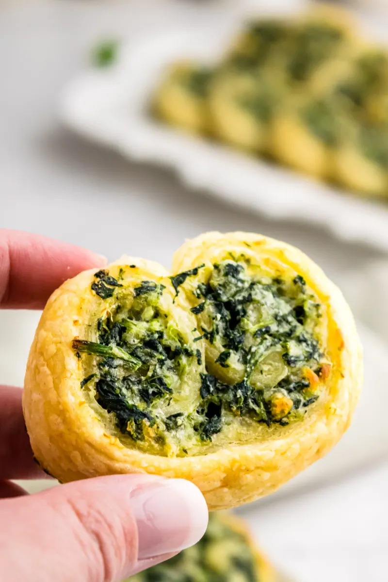 fingers holding one spinach palmier appetizer