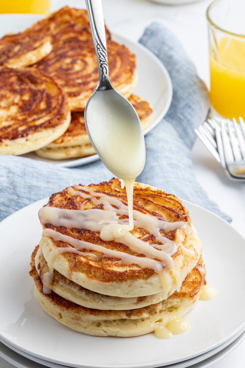 pouring icing onto maple cinnamon roll pancakes