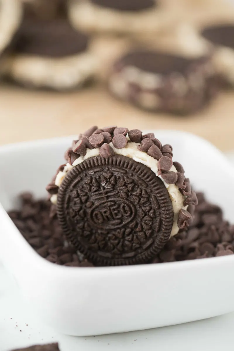 rolling chocolate chip cookie dough stuffed oreos in more chocolate chips in a white dish