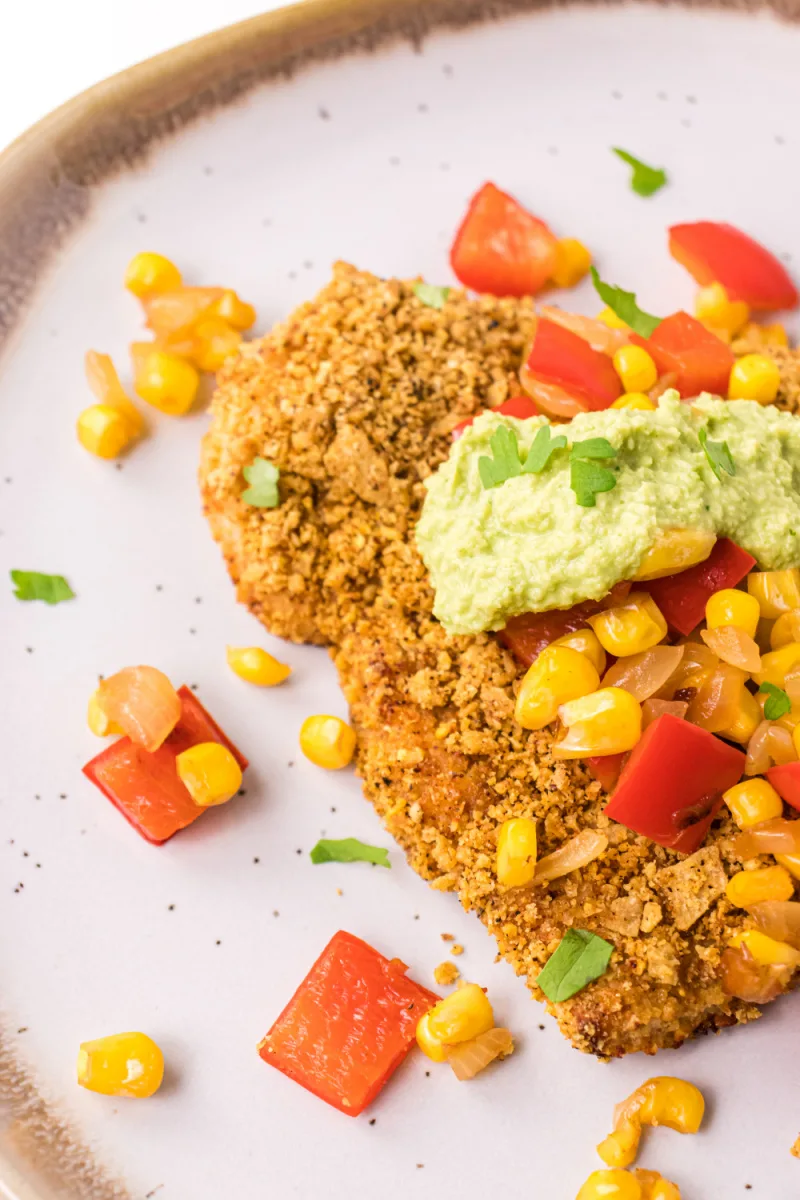 tortilla crusted turkey cutlets on a plate topped with salsa and avocado