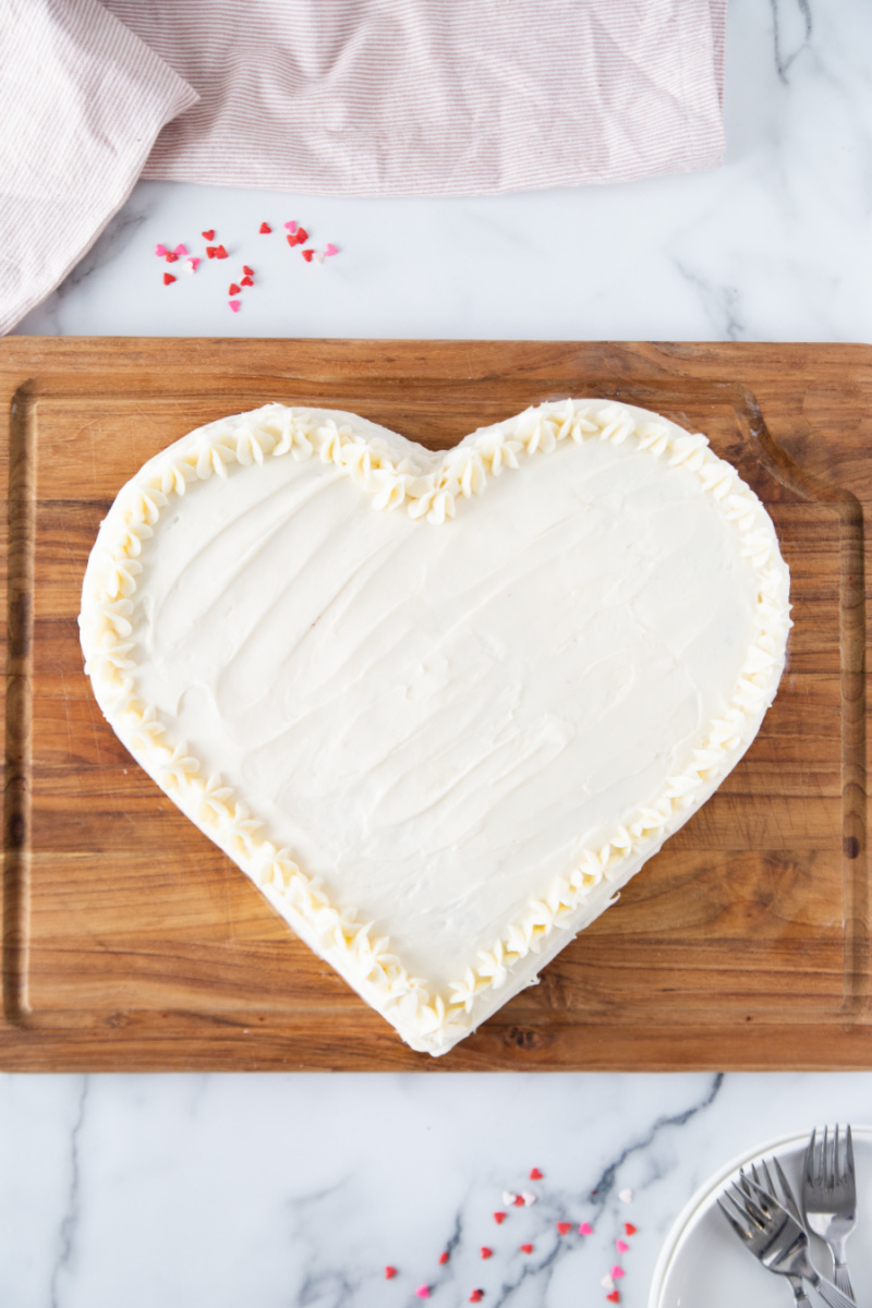 heart shaped cake with white frosting on a cutting board
