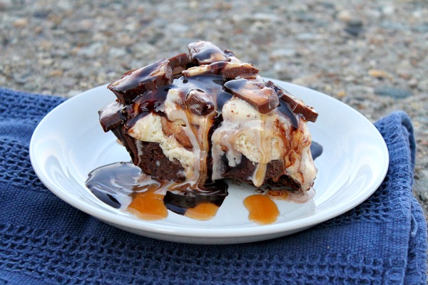 slice of Snickers Ice Cream Brownie Pie on a white plate with a blue napkin