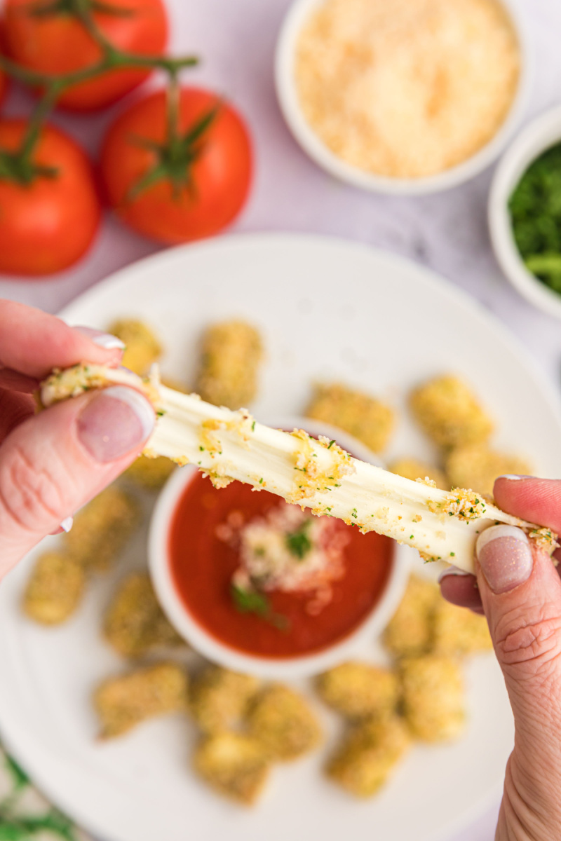 fingers pulling apart mozzarella bite to show gooey cheese