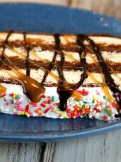 slice of ice cream sandwich cake topped with caramel and hot fudge on a blue plate