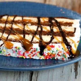 slice of ice cream sandwich cake topped with caramel and hot fudge on a blue plate