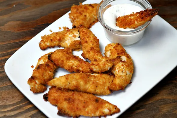 baked parmesan chicken tenders on a white plate served with a glass dish of ranch dressing