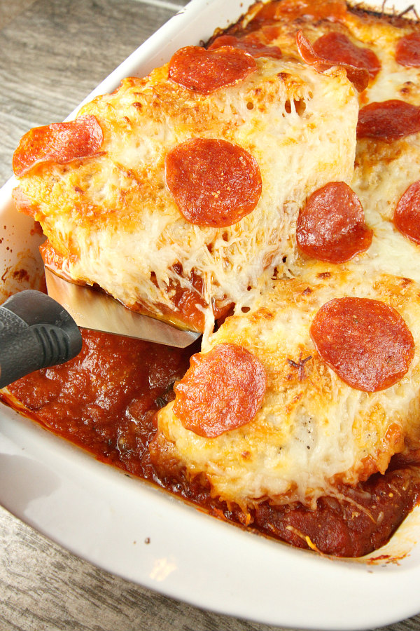 using a spatula to serve chicken pizzaiola from a white casserole dish