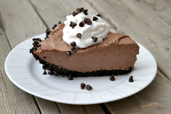 slice of nutella pie with whipped cream and chocolate chips served on a white plate on a wooden board