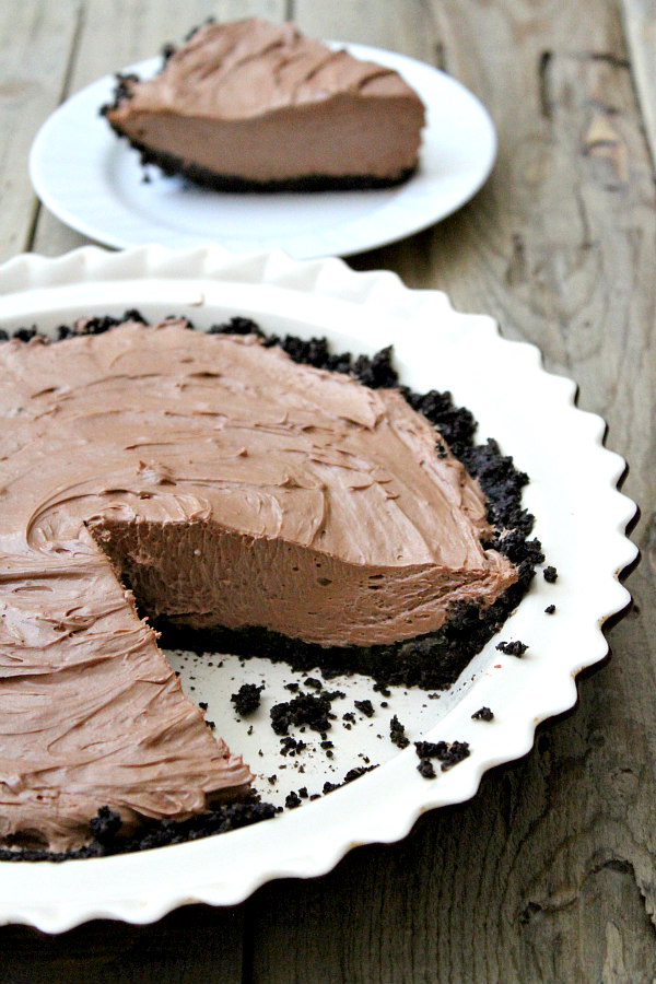 No bake nutella pie in a white pie plate with a slice cut out of it and the slice on a white plate in the background