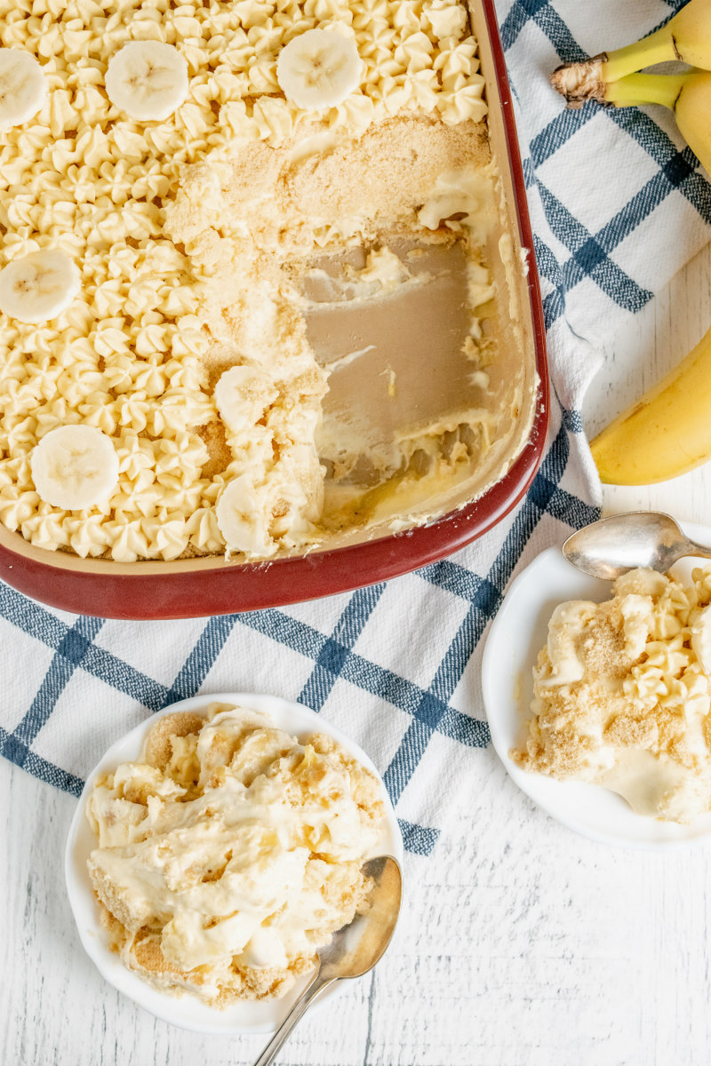 serving banana pudding from a serving dish onto white plates on a blue plaid napkin