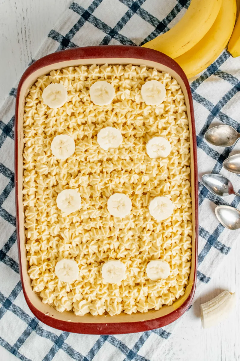 banana pudding in a serving dish on a blue plaid napkin with silver spoons