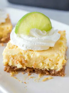 key lime bar on a white plate garnished with whipped cream and a lime wedge