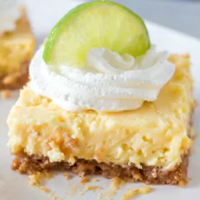 key lime bar on a white plate garnished with whipped cream and a lime wedge