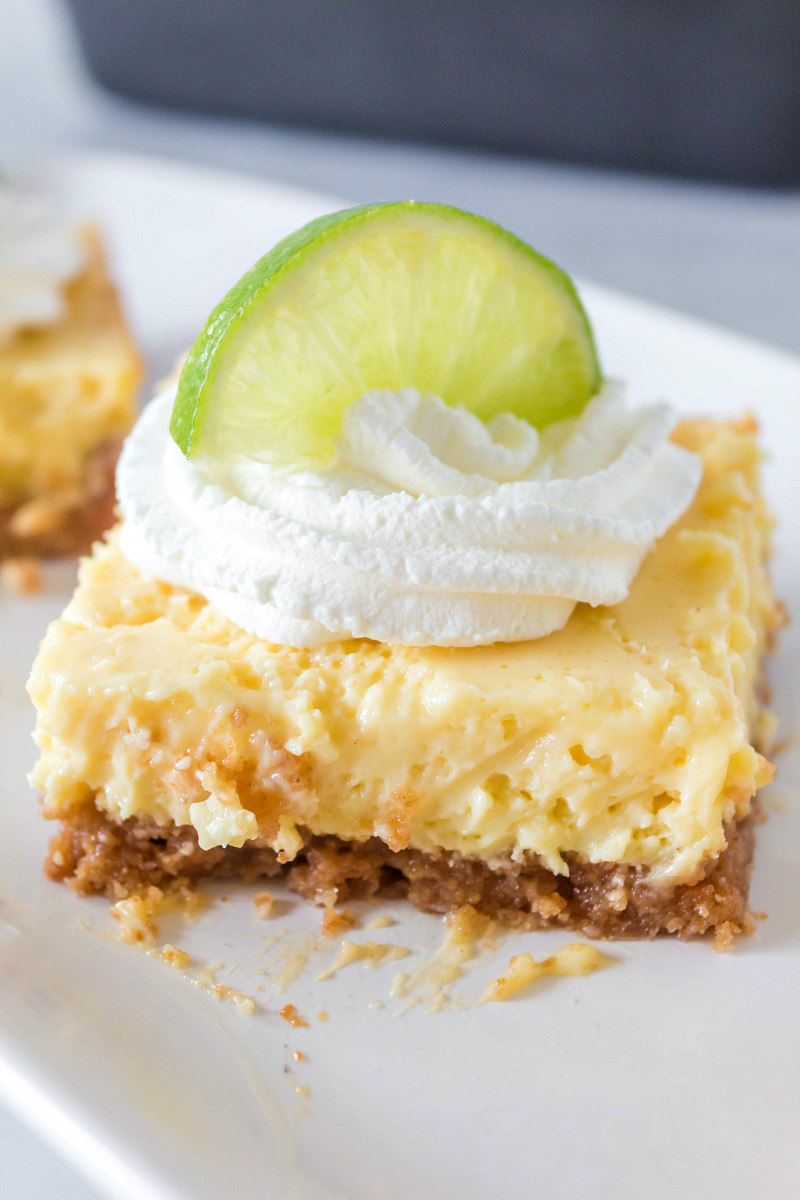 key lime bar on a white plate garnished with whipped cream and a lime wedge