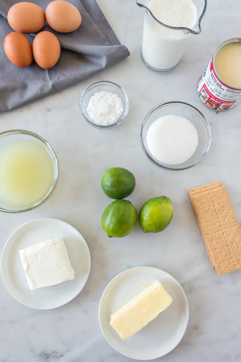 overhead shot of ingredients needed for key lime bars on a white background and displayed in glass bowls