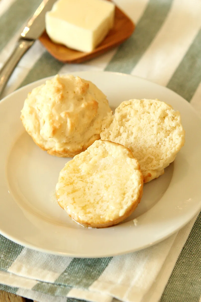 No Yeast Dinner Rolls on a white plate with a green and white striped napkin. Roll is cut open and served with butter.