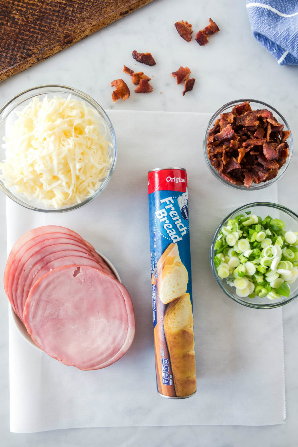overhead shot of ingredients displayed for stromboli- ham, cheese, bacon, green onions and french bread loaf