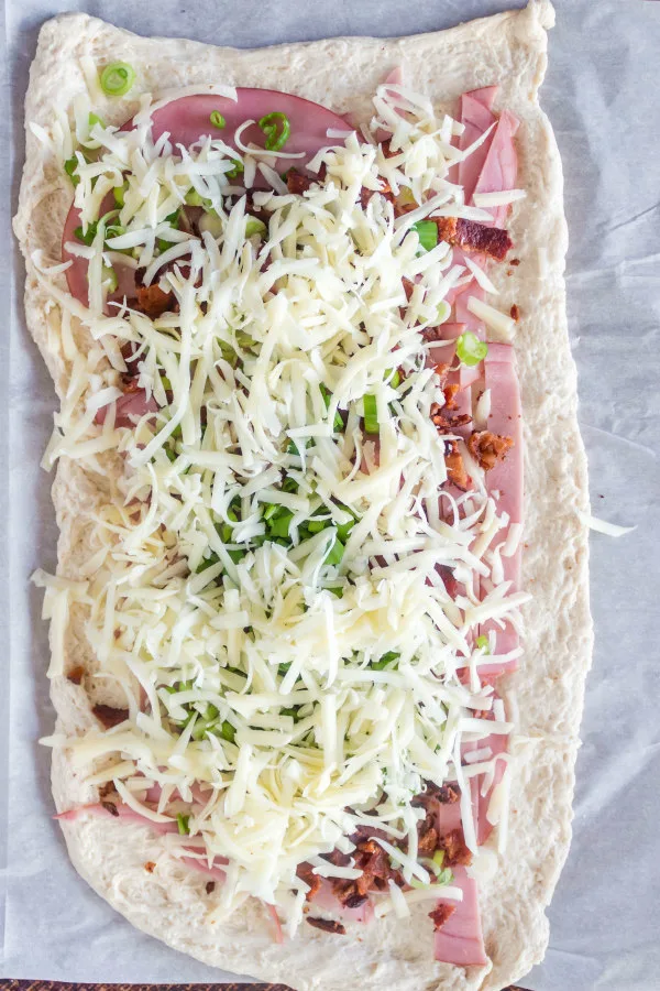 rolled out dough with ham and swiss cheese and other stromboli ingredients spread on top