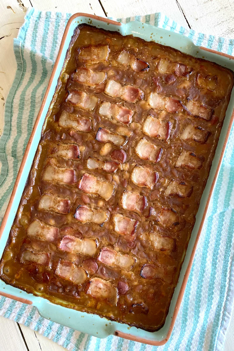 overhead shot of barbecue beans cooked in a casserole dish set on a blue and white striped dishtowel