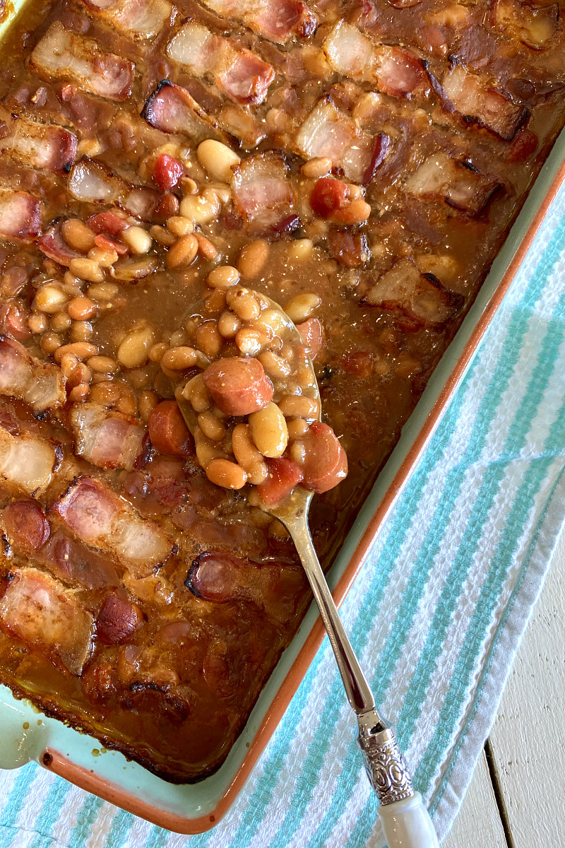 barbecue beans in a blue casserole dish with a serving spoon set on a green and white striped dishtowel