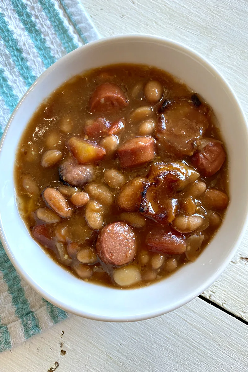 white serving bowl filled with barbecue beans with a blue and white dishtowel on the side