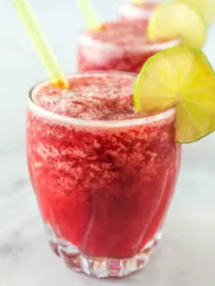 three cherry lime slushies garnished with lime and with a straw