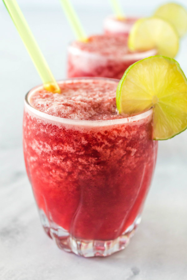 three cherry lime slushies garnished with lime and with a straw