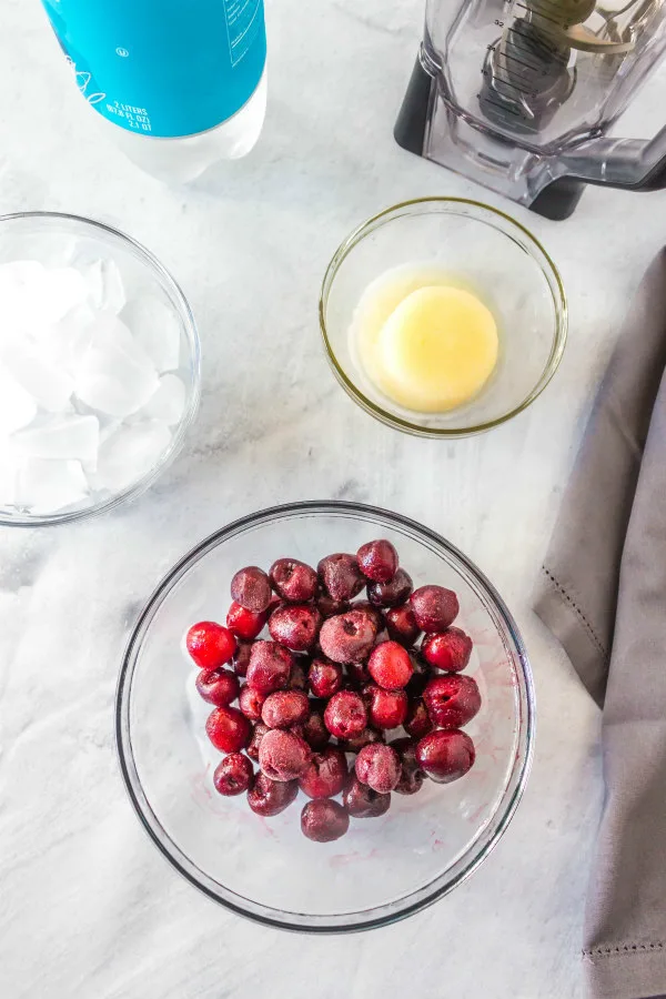 ingredients displayed for cherry lime slushies in glass bowls: cherries, powdered sugar, frozen limeade