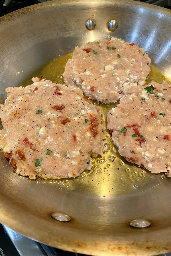 chicken and sun dried tomato burgers frying in a skillet