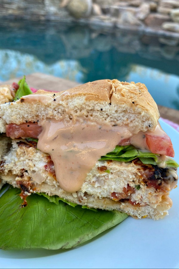 chicken and sun dried tomato burgers cut in half to see the inside with sauce dripping down on a white plate with a backyard pool background