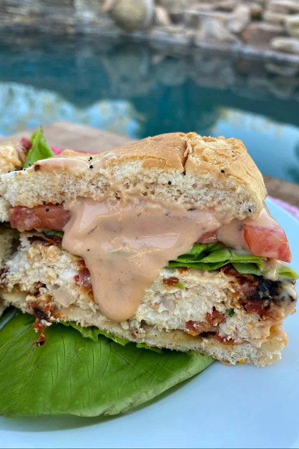 chicken and sun dried tomato burgers cut in half to see the inside with sauce dripping down on a white plate with a backyard pool background