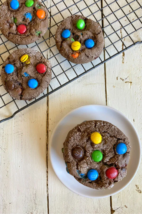 Chocolate cake mix M&M cookies on a cooling rack with a small white plate with a cookie on it alongside