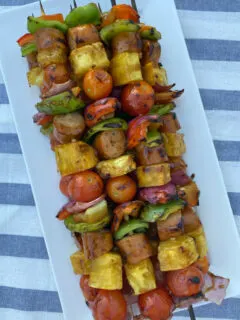 hawaiian chicken sausage kabobs stacked on a white platter set on a white/blue striped napkin