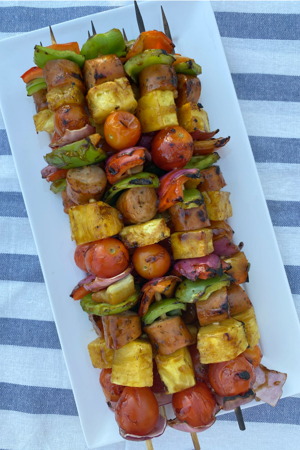 hawaiian chicken sausage kabobs stacked on a white platter set on a white/blue striped napkin