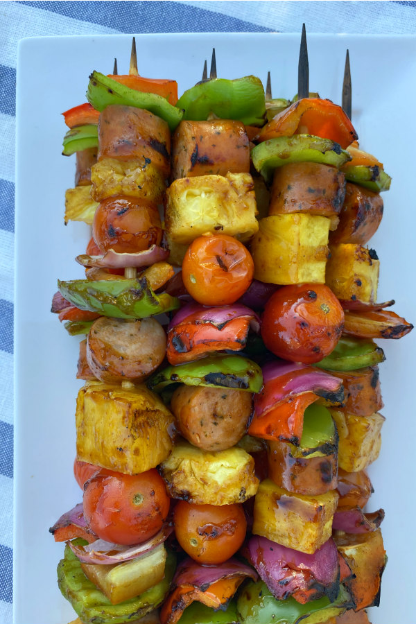 hawaiian chicken sausage kabobs stacked on a white platter set on a white/blue striped napkin