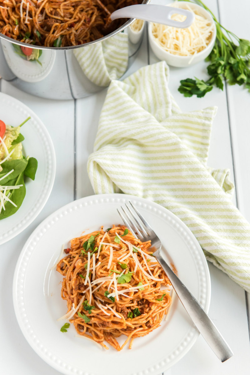 spaghetti on a white plate with pot of spaghetti in background