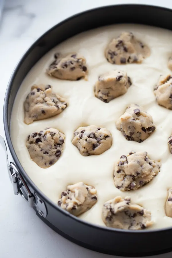 cheesecake batter in a cheesecake pan with balls of chocolate chip cookie dough dropped into the batter