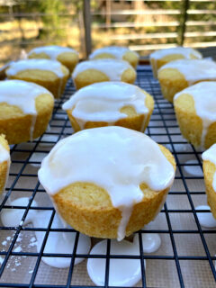 glazed lemon muffins on a rack with the glaze dripping off the sides of the muffins