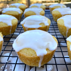 glazed lemon muffins on a rack with the glaze dripping off the sides of the muffins