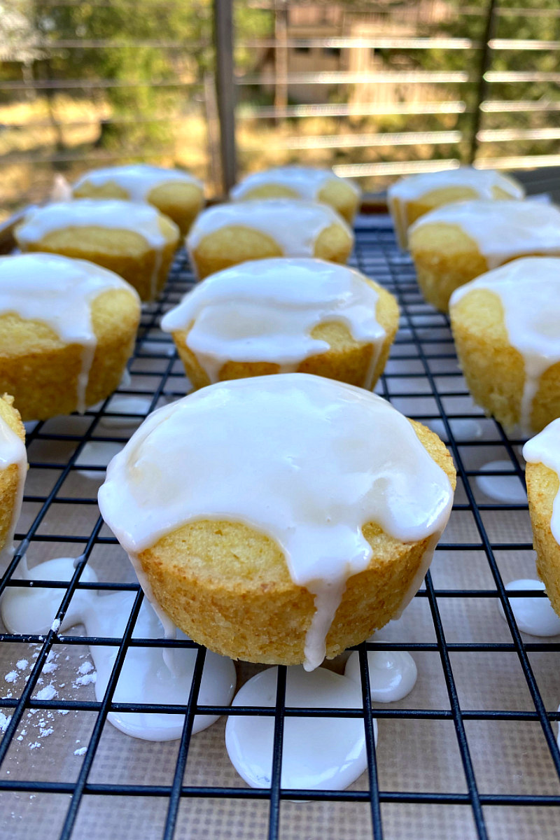 glazed lemon muffins on a rack with the glaze dripping off the sides of the muffins