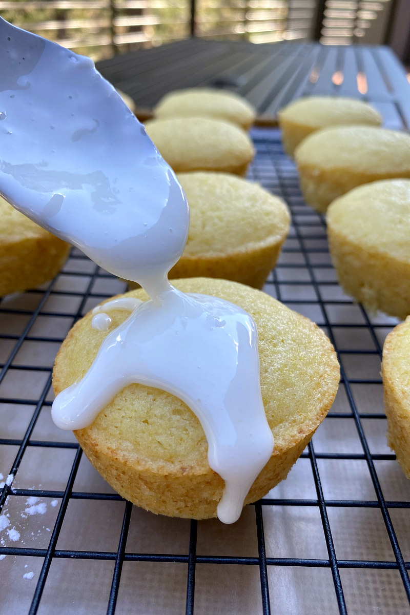 spooning glaze onto lemon muffins set on a rack