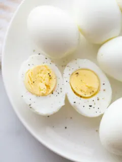 hard boiled eggs cut in half and displayed on a white plate with other whole hard boiled eggs. sprinkled with salt and pepper.